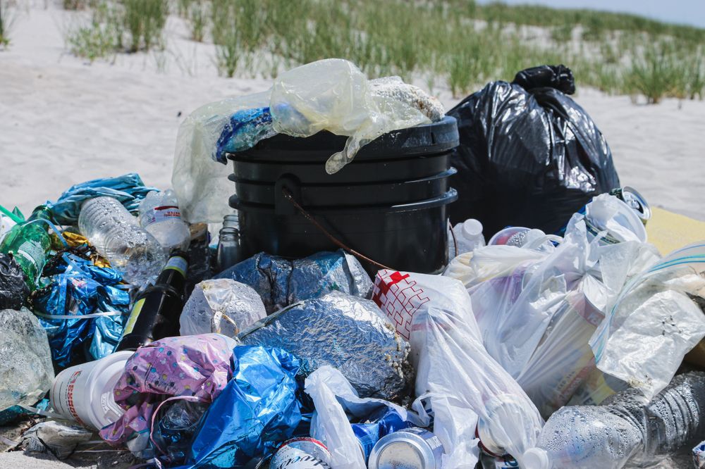 Overflowing trash can on a beach with plastic bags and bottles