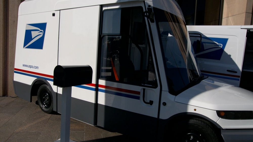Electric USPS delivery van next to a mailbox
