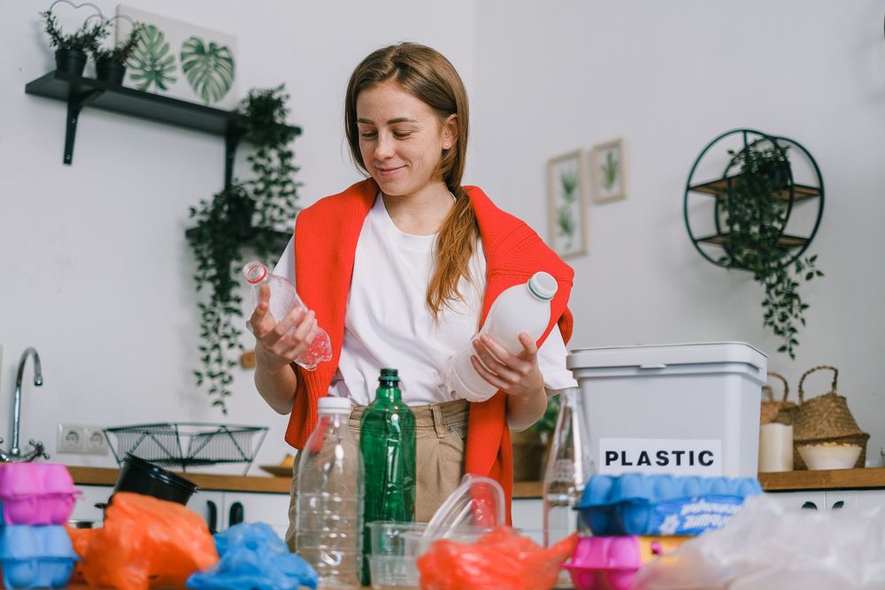 Person sorting through waste, with a bin labeled &quot;plastic&quot; nearby